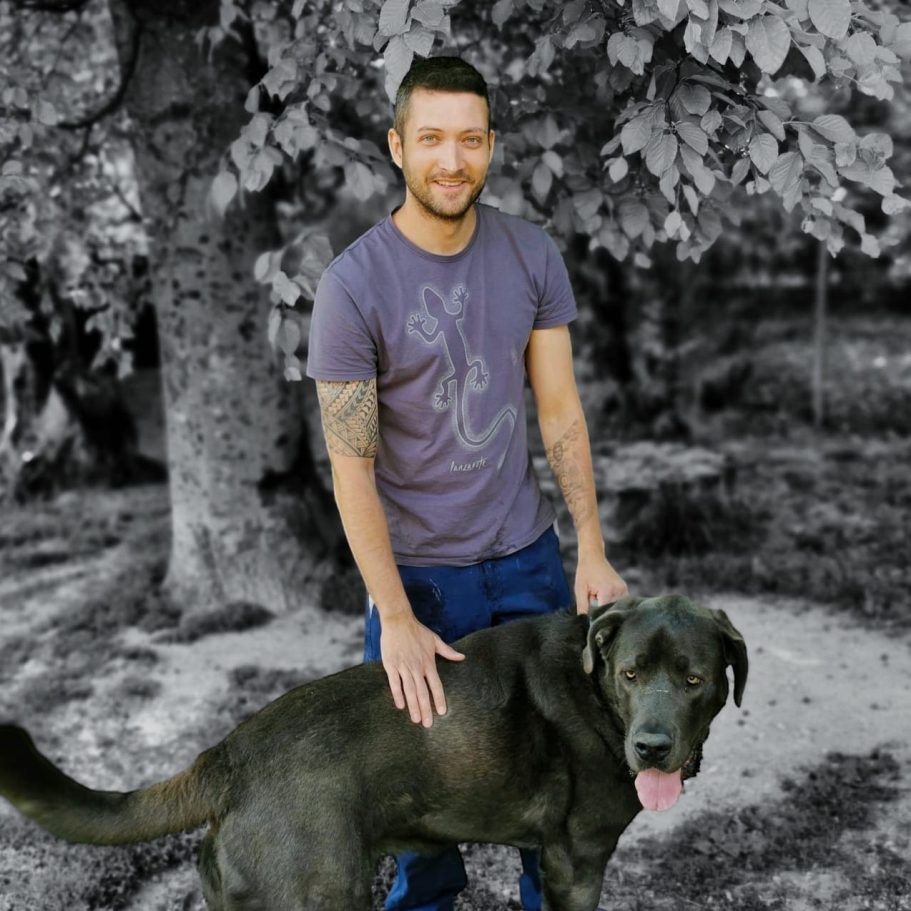 Robert Steinberger Ein Mann steht neben einem schwarzen Hund in einem bewaldeten Bereich.