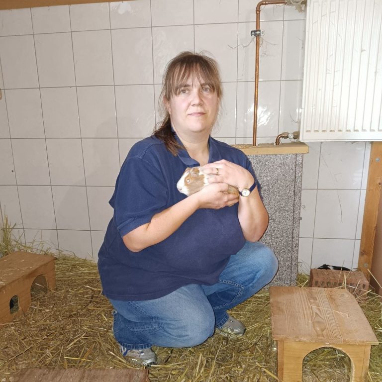Stefanie Wittig Frau mit einem Meerschweinchen in den Händen, in einem Raum mit Stroh.