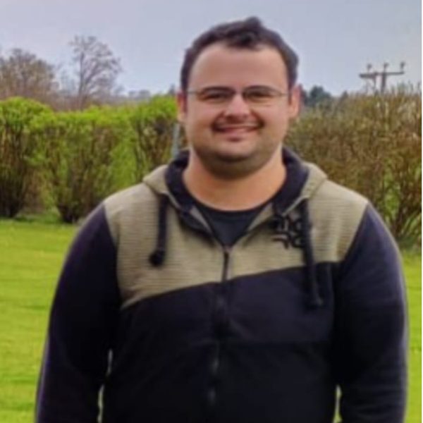 Johannes Bosch Mann mit Brille, in lässiger Kleidung, steht im Freien vor einer bewachsenen Landschaft.
